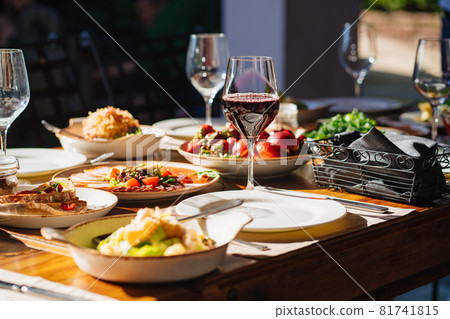 wooden table served with plates with salad and snacks on the open terrace wooden table served with plates with salad and snacks on the open terrace 81741815