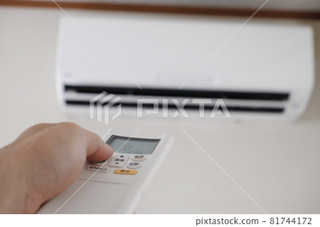 Image of operating an air conditioner with a remote control held in hand 81744172