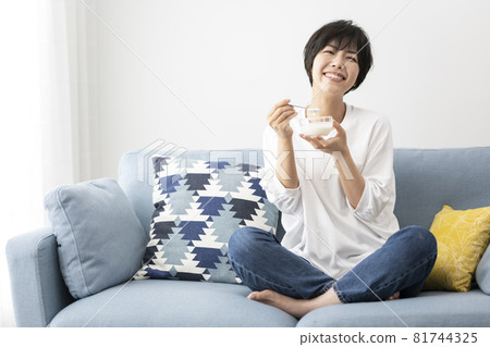 Young woman eating yogurt on the sofa in the room 81744325