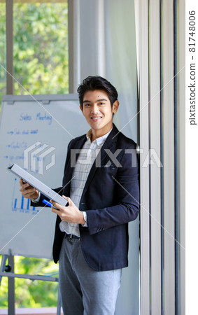 Asian successful professional happy handsome male employee sales marketing officer in casual suit standing smiling look at camera hold document folder and marker in front whiteboard in meeting room Asian successful professional happy handsome male employee sales marketing officer in casual suit standing smiling look at camera hold document folder and marker in front whiteboard in meeting room 81748006