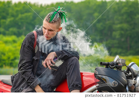 a guy with dreadlocks on his head smokes vape on a motorcycle 81751927