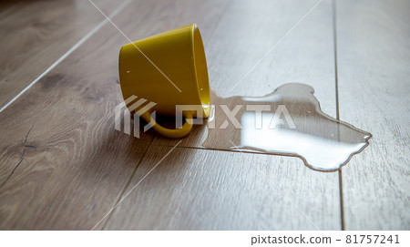 Yellow cup of water spilled on a wooden laminate floor. Moisture protection of a floor. Waterproof parquet board with spilled water. Yellow cup of water spilled on a wooden laminate floor. Moisture protection of a floor. Waterproof parquet board with spilled water. 81757241