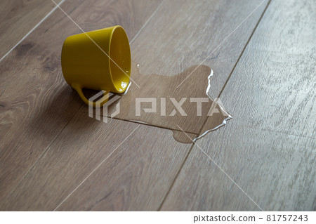 Yellow cup of water spilled on wooden laminate floor. Moisture protection of a floor. Parquet board with spilled water. Yellow cup of water spilled on wooden laminate floor. Moisture protection of a floor. Parquet board with spilled water. 81757243