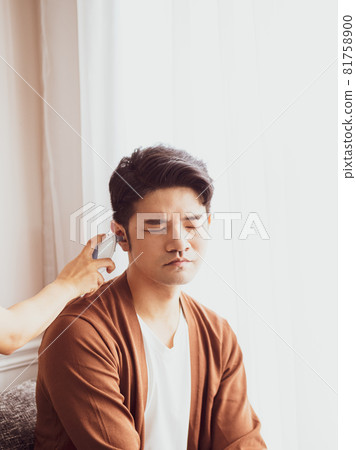 Young Asian man wearing surgical mask and using ear thermometer to measure body temperature 81758900