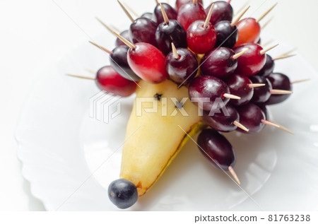 Fruit hedgehog, red grapes and juicy pear, creative way of serving fruit Fruit hedgehog, red grapes and juicy pear, creative way of serving fruit 81763238