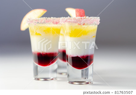 Three layered shot drink based on liqueur, cream and apple peach juice, decorated with colored sugar and a slice of apple 81763507