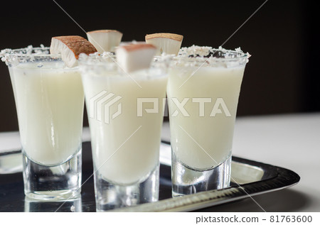 Coconut cocktail in drink shot glass based on the rum decorated with coconut flakes served on a silver tray Coconut cocktail in drink shot glass based on the rum decorated with coconut flakes served on a silver tray 81763600