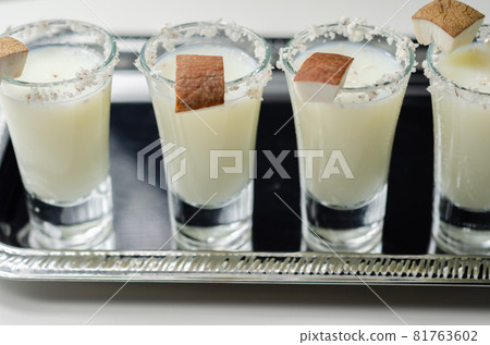 Coconut cocktail in drink shot glass based on the rum decorated with coconut flakes served on a silver tray Coconut cocktail in drink shot glass based on the rum decorated with coconut flakes served on a silver tray 81763602