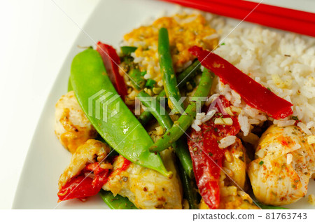 Chicken breast pieces in a Thai red curry sauce made with coconut cream, red chillies, lemongrass, lime leaf, with fragrant rice, red peppers, mange tout, and green beans 81763743