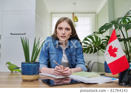 Online training, female teenager sitting at home looking at webcam, Canadian flag on table Online training, female teenager sitting at home looking at webcam, Canadian flag on table 81764141