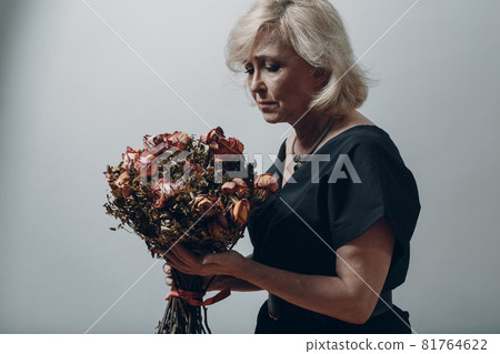 Upset elderly woman hold withered dry old rose flowers bouquet. 81764622