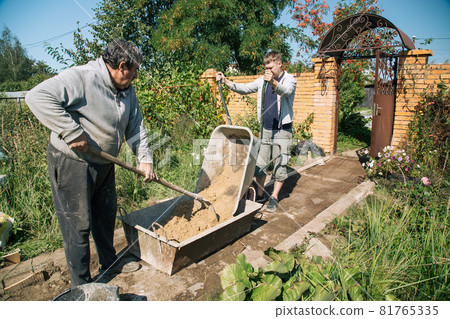 A man unloads sand into a cement mixture for pouring a garden path 81765335
