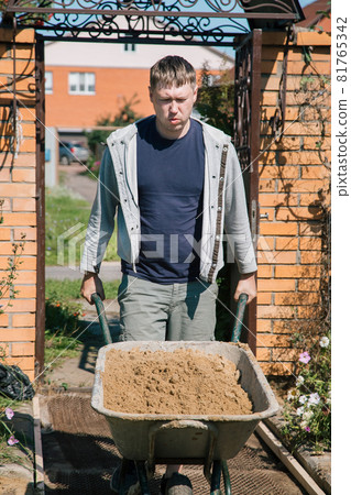 A man unloads sand into a cement mixture for pouring a garden path A man unloads sand into a cement mixture for pouring a garden path 81765342