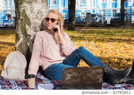 Young woman working with laptop outdoors and holding phone Young woman working with laptop outdoors and holding phone 81765651