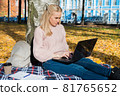 A young woman works in a park, typing on a laptop 81765652