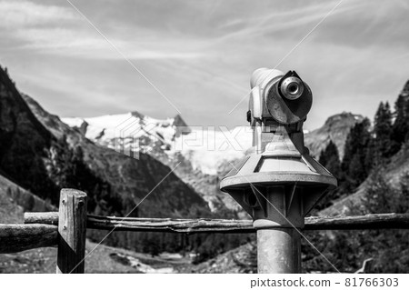 Touristic telescope in alpine valley for watching surrounding mountains and glacier. Grossvenediger lookout point, Hohe Tauern National Park, Austrian Alps. Black and white image. 81766303