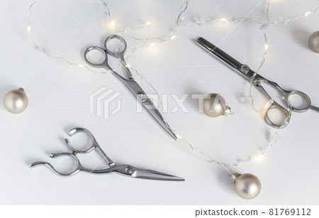 Hairdressing scissors and Christmas balls, lights on a white table, top view 81769112