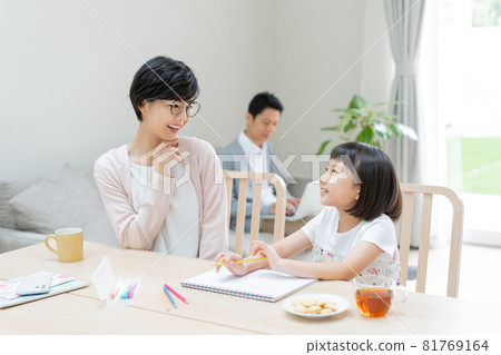 A little girl draws and her mother watches her, while her father works on the computer on the sofa 81769164