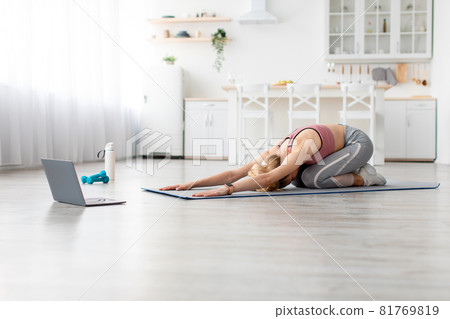 European millennial blonde sportswoman doing body stretching and watching online workout lesson on laptop at home European millennial blonde sportswoman doing body stretching and watching online workout lesson on laptop at home 81769819