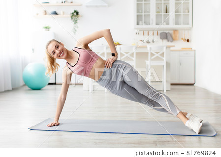Happy caucasian beautiful millennial blonde fitness blogger lady doing exercise side plank on mat Happy caucasian beautiful millennial blonde fitness blogger lady doing exercise side plank on mat 81769824