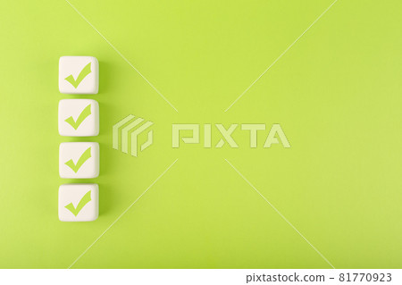 Four checkmarks on white cubes against bright green background with copy space 81770923