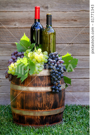Various colorful grapes and wine bottles on wine barrel Various colorful grapes and wine bottles on wine barrel 81771343