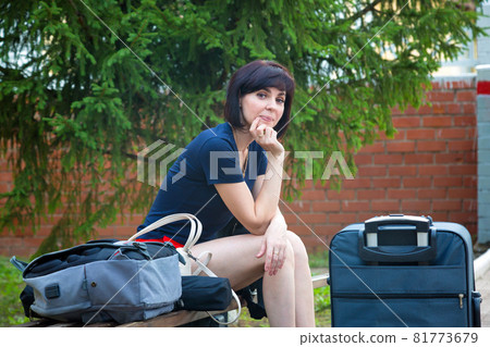 A bored woman on a bench with a suitcase at the train station waiting for her train A bored woman on a bench with a suitcase at the train station waiting for her train 81773679