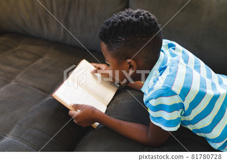African american boy reading book and lying on couch in living room 81780728