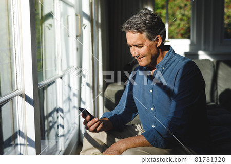 Happy senior caucasian man in living room sitting on sofa, using smartphone Happy senior caucasian man in living room sitting on sofa, using smartphone 81781320