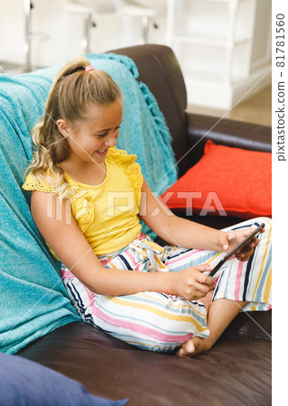 Laughing caucasian girl sitting on couch and using tablet in living room Laughing caucasian girl sitting on couch and using tablet in living room 81781560