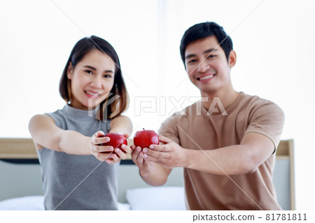 Positive ethnic couple with apples in bedroom 81781811