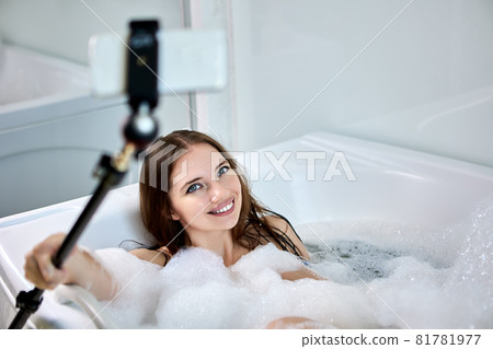 Woman takes pictures of herself in bathtub using smartphone and selfie stick. Woman takes pictures of herself in bathtub using smartphone and selfie stick. 81781977