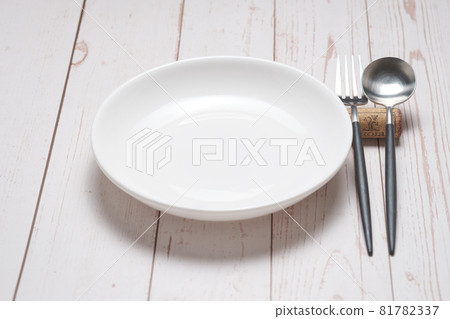White round plate, spoon and fork on a white table White round plate, spoon and fork on a white table 81782337