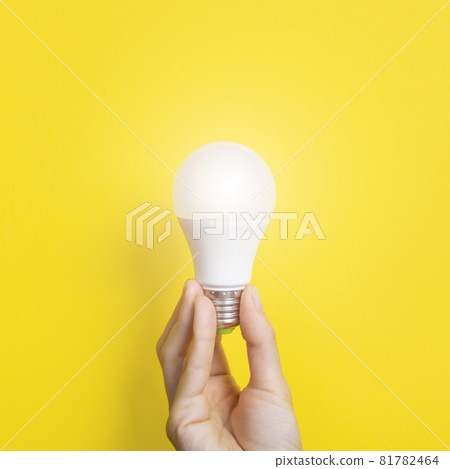 Hand holding a LED light bulb on bright yellow background. Using economical and environmentally friendly light bulb concept. Idea concept. Energy saving lamp in woman's hand Hand holding a LED light bulb on bright yellow background. Using economical and environmentally friendly light bulb concept. Idea concept. Energy saving lamp in woman's hand 81782464