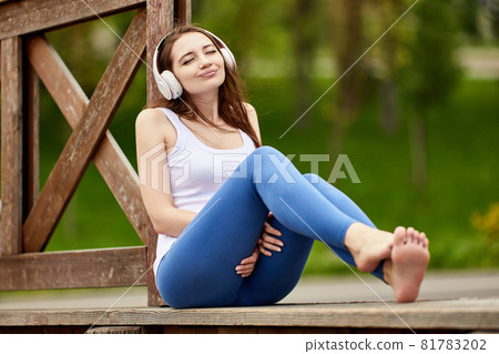 Woman in wireless headphones closed her eyes while listening to music in nature. Woman in wireless headphones closed her eyes while listening to music in nature. 81783202