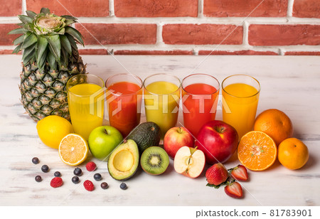 Different fruits juice in glass, apple, orange and strawberry juice with straw, looking refreshing on colourful wood board in front of brick wall background. Picture decorating with fresh fruits Different fruits juice in glass, apple, orange and strawberry juice with straw, looking refreshing on colourful wood board in front of brick wall background. Picture decorating with fresh fruits 81783901