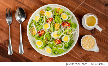 Big white bowl of lettuce, sprout salad with boil egg, onion and tomato mix with Japanese sesame oil dressing on wooden table together with small olive oil jar and sesame cup and utensil beside Big white bowl of lettuce, sprout salad with boil egg, onion and tomato mix with Japanese sesame oil dressing on wooden table together with small olive oil jar and sesame cup and utensil beside 81783962