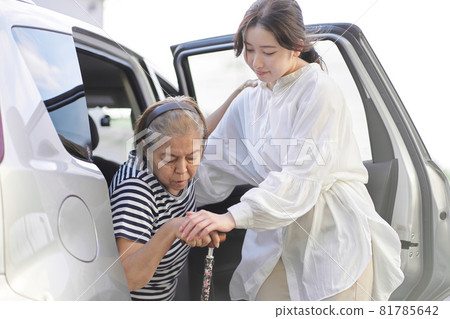 A woman helping an elderly person out of a car A woman helping an elderly person out of a car 81785642