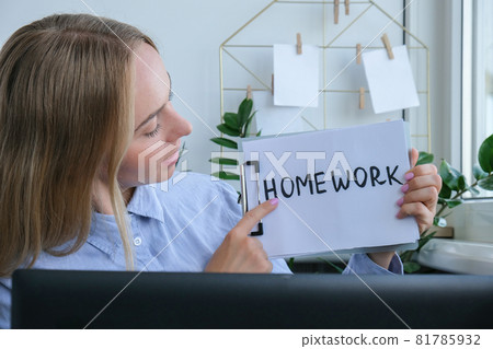 Young female teacher sitting at desk and using laptop showing HOMEWORK text at home. e Education Back to school. Student learning online class. Distance learning. Exam preparation 81785932