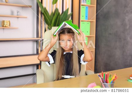 Portrait of a girl in a school uniform with a book in her hands. The child reads a textbook. Preparing a schoolgirl for a school lesson or exam 81786031