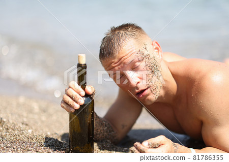 Drunk man on beach with closed eyes holding bottle of wine Drunk man on beach with closed eyes holding bottle of wine 81786355