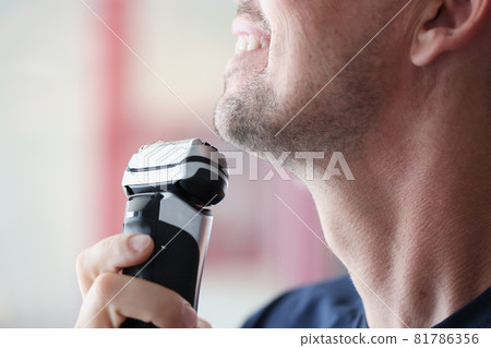 Young man shaves with electric razor closeup 81786356