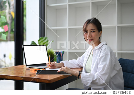 Young female entrepreneur sitting at modern workplace and smiling to camera. 81786498