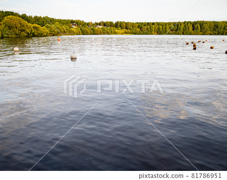 calm water surface of lake with floating buoys and a forest on horizon at September sunset calm water surface of lake with floating buoys and a forest on horizon at September sunset 81786951