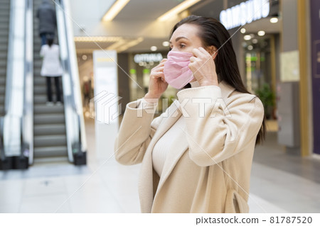 woman puts on a medical protective mask in a public place woman puts on a medical protective mask in a public place 81787520