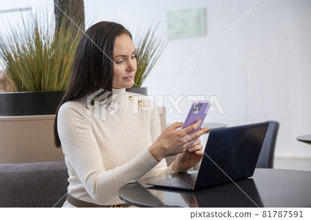 beautiful business woman typing on the phone while sitting at the table with laptop beautiful business woman typing on the phone while sitting at the table with laptop 81787591