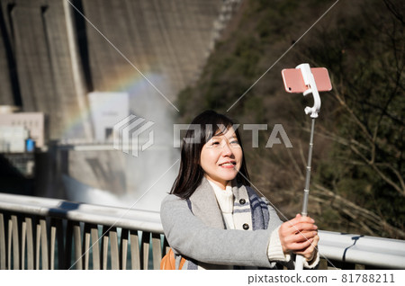 A woman taking a selfie with the rainbow over the dam in the background 81788211