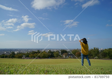 一個女人在後面,她的手舉在草地上的草地上,藍天下,在公園裡,可以看到風景 一個女人在後面,她的手舉在草地上的草地上,藍天下,在公園裡,可以看到風景 81789750