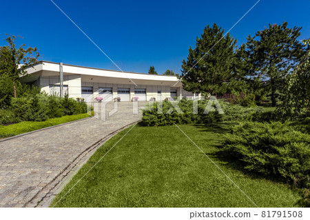 Modern garage for several cars with paved driveway surrounded by green parkland Modern garage for several cars with paved driveway surrounded by green parkland 81791508