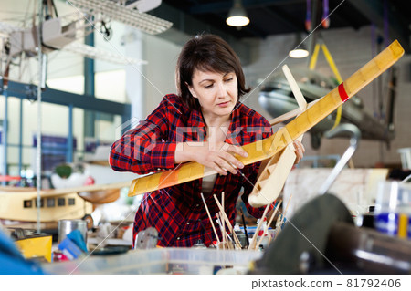 Female aircraft enthusiast engaged in creating plane models in workshop 81792406
